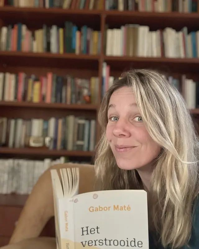 Mirthe van Liere voor haar boekenkast, met een boek van Gabor Maté